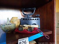 Photo showing vintage opera glasses with mother of pearl inlay on a red cloth pouch, antique cast iron iron, and two ceramic vases placed on a wooden shelf