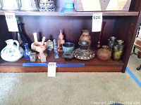Shelf display showing a variety of ceramic, glass, and metal vases and figurines with traditional patterns and designs.