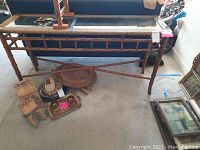 Full view of wicker-trimmed Rafferty sofa table with glass top, wooden trunk underneath, and some decorative smaller items on the floor beside them.
