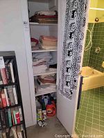 Photo showing a cabinet with shelves containing various folded linens and fabric pieces, cleaning supplies like liquid detergent and spray bottles are on the bottom shelf.