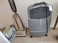 Photo showing Honeywell CO30XE swamp cooler and Panasonic Jet-Flo MC-6255 upright vacuum side by side on carpet.