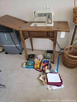 Singer sewing machine installed in a wooden table with sewing accessories arranged in front including spools of thread, scissors, and fabric pieces.