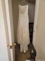 Full view of 1950s strapless satin wedding gown hanging, showing its length and train.