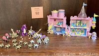 Wide view showing two miniature play sets: a pink castle with figures and a collection of medieval figures and horses including a purple dragon.