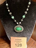 View of the full adjustable choker necklace on a black velvet display showing the green gemstone pendant surrounded by rhinestones and beaded chain with green and silver beads.