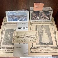 Assorted vintage ephemera laid out on a flat surface including magazines, sheet music, and photo cards in protective sleeves.