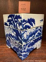 Front and angled view showing the stacked two square ceramic boxes with blue and white painted landscape design featuring pine trees, mountains, and water.