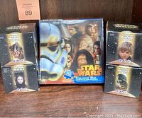 Four sealed Star Wars Episode 1 collectible figurines in original black promotional boxes alongside the Disney Star Wars Saga lenticular puzzle in its box.