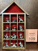 Wooden house-shaped frame with 12 compartments holding metal animal figurines, red velvet backing visible