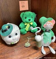 Full view of all four vintage St. Patrick's Day collectibles including ceramic piggy bank, plush teddy bear, fabric mouse figurine, and jeweled keychain.