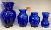 Four blue glass vases of different sizes and shapes arranged side-by-side showing color and shape