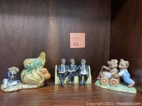 Photo of three vintage collectible figurines on a wooden shelf: two bears with a wagon, three men sitting on a bench, and a man with a green elephant.