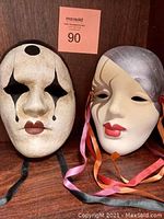 Two decorative hand-painted masks displayed side by side, showing front view of both masks.
