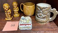 Full lot showing two tiki salt and pepper shakers, a brown tiki mug, and a shell-covered trinket box.