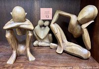 Three hand carved wooden abstract figurines: two of seated thinking men and one loving couple embracing in heart shape, all without lower backs/spines.
