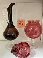 Photo of plum glass carafe, rose glass stemmed round belly vase, and rose glass sleeping kitty candle holder
