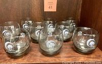 Nine smoked low ball glasses featuring etched Los Angeles Rams helmet logos arranged in a display case.