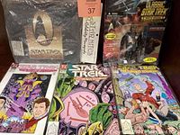 Photo showing the three sealed Star Trek The Tabukan Syndrome comic books and the sealed 30 Year Anniversary mouse pad alongside the sealed Classic Star Trek action figure with galactic accessories on card.