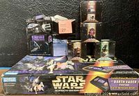 Photo showing the full lot including the Star Wars Interactive Video Board Game box on the bottom with various collectible boxes stacked above it against a black background.