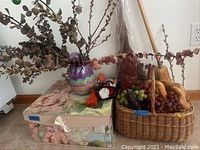 Overall view showing floral nesting boxes, ceramic vase with plant arrangement, two woven fruit baskets with artificial fruit and decorative brooms in background