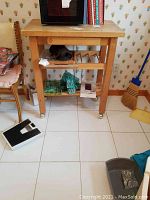 Full view of wooden butcher block cart showing top, drawer, two shelves on caster wheels in a room with wallpaper and various items nearby.