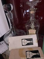 Two glass decanters displayed with one labeled 'Colonial Decanter' and two boxes of wine markers in front.