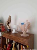 Photo on shelf showing wooden sculpture, milk glass goblet, and peach bowl with nude figure