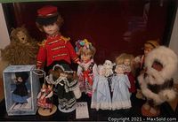 Wide group shot of 12 dolls including Cowardly Lion and a large red uniformed doll on a dark background