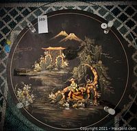 Top view of the round table showing the hand painted Asian-inspired landscape scene and the layered glass top with apparent damage.