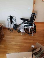 Overall photo showing manual wheelchair, silver folding walker with wheels and gray foam hand grips, and sitting/standing support strap.