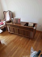 Full front and side view of the stereo console in a room with hardwood floor, showing overall wood cabinet, drawers, and speaker grills.
