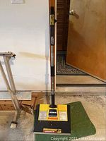 Front view of the Noma snow shovel showing the aluminum handle with grip and yellow-black plastic shovel head with label.