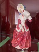 Full side view of Royal Doulton porcelain figure dressed in red and white holding a parcel.