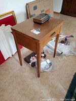 Wooden sewing machine table from front angle, showing drawer and scratches