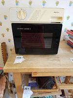 Front view of Sharp Half Pint Carousel microwave oven sitting on a wooden table, showing control panel with dial and cooking instructions, black door with window.
