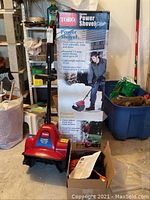 Front view of red Toro Electric Power Shovel Plus device in front of the original product box with usage details and features.