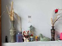 Shelf with seven decorative items including two vases with dried flowers, ceramic Happy Cat, green dragon lustreware jar, decoy duck, birdhouse, and purple covered jar.