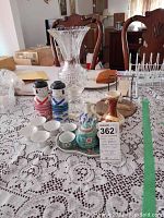 Full view of table displaying the cut glass vase, saki decanters and cups, Delft pitcher, brown ceramic vase, and Chinese porcelain tea set with tag on table
