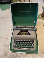 Royal Senior Companion manual typewriter inside original clamshell hard case with green interior, light outer shell, situated on a concrete floor.