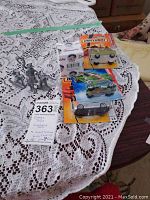 Three packaged die-cast cars and four lead figurines displayed on a lace tablecloth.