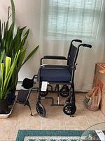 Side angled view of manual wheelchair showing navy blue cushioned seat, black frame, armrests, and footrests.