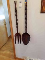 Full view of carved wood decorative fork and spoon mounted on a wall, showing length and overall shape.