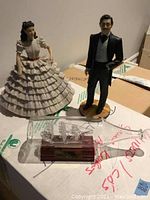 Photo showing two Gone with the Wind figurines—Scarlett O'Hara and Rhett Butler, alongside a glass bottle containing a model ship resembling the Santa Maria.