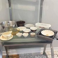 Photo showing variety of kitchen items including aluminum tube pan, Pyrex loaf dish, bowls, baking tins, and gravy boat arranged on a shelf.