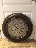 Photo showing the large round wall clock with dark brown resin frame and decorative Roman numeral clock face.