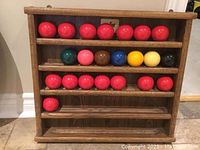 Wooden rack holding 22 snooker balls arranged across shelves including red and colored balls