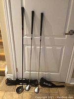 Three golf clubs standing vertically with their corresponding protective covers laid in front, showing multiple brands and loft details.