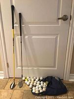 Wilson SW sand wedge golf club and Loco #5HB golf club standing upright with a pile of used golf balls in front, all placed against a white door indoors.