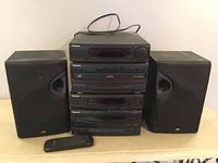 Full view of Panasonic stacked stereo system with two black JVC bookshelf speakers and remote control placed on table.