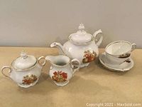 White ceramic tea set items including teapot, creamer, sugar bowl, two cups and two saucers shown on table.